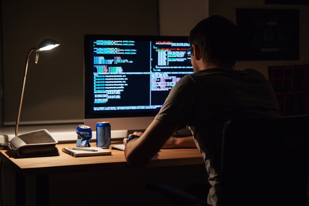 Back view of modern programmer sitting and writing code in dark room