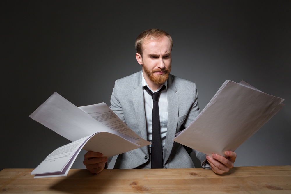 Portrait of a handsome businessman sitting at the table and reading papers over dark background