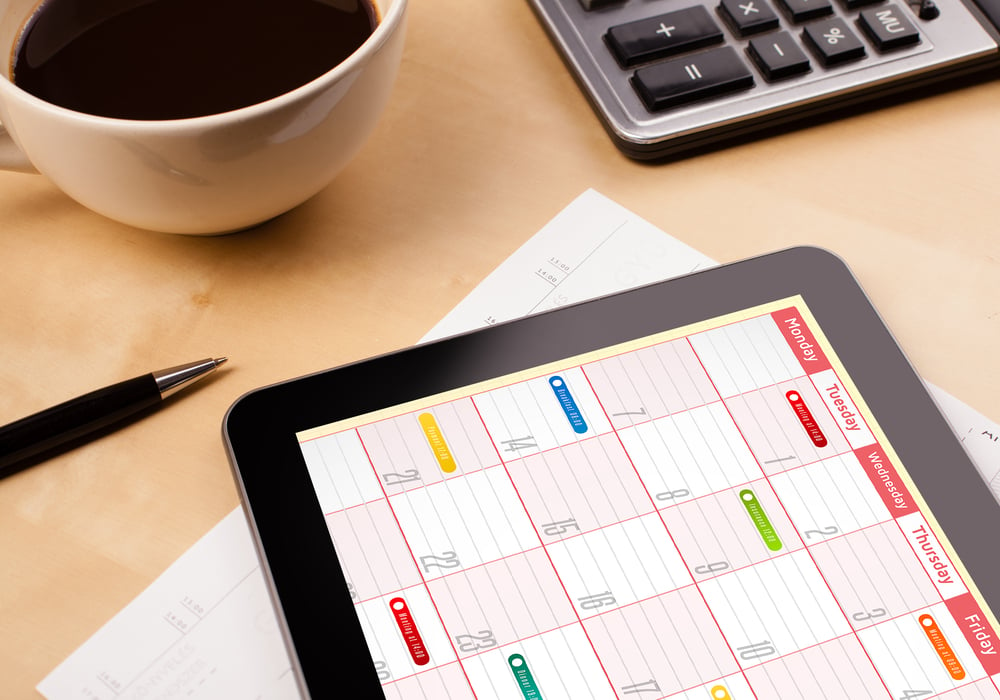 Workplace with tablet pc showing calendar and a cup of coffee on a wooden work table close-up