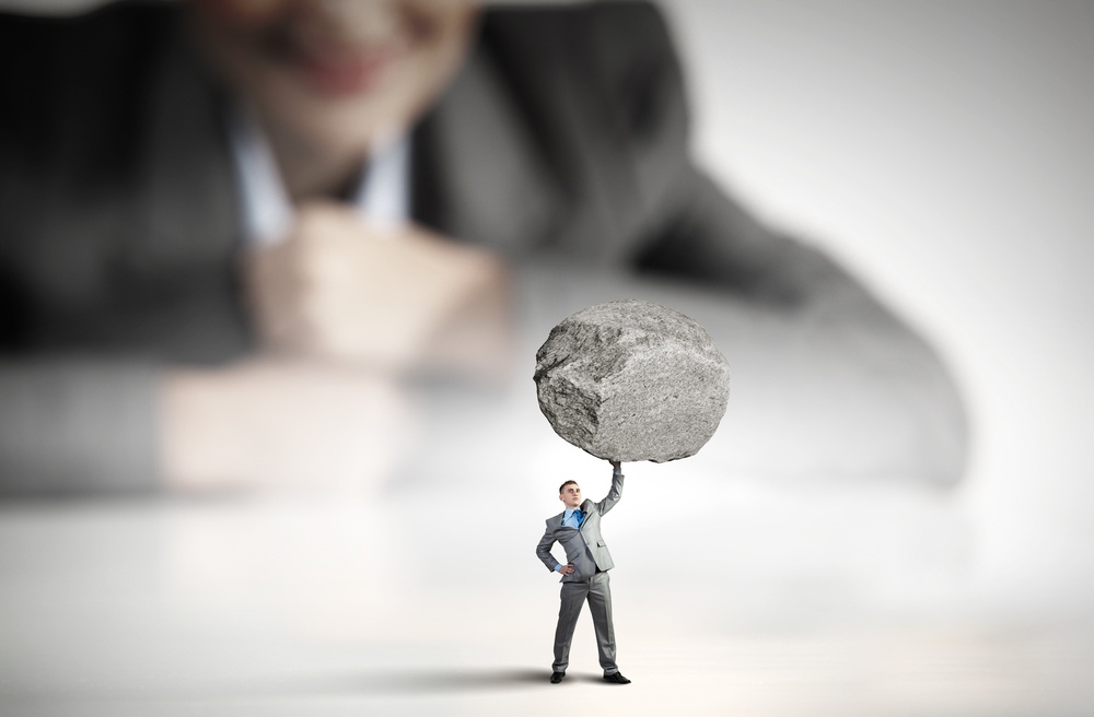 Businesswoman looking at miniature of businessman lifting stone above head.jpeg